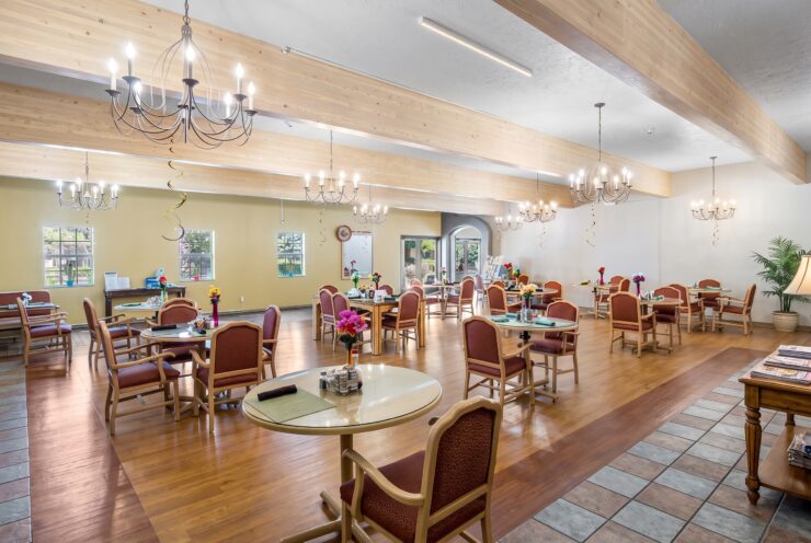 Spacious dining room with warm lighting, comfortable seating, and floral table accents fostering community.