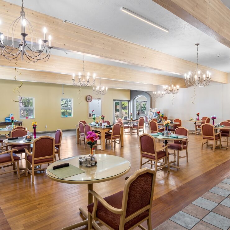 Spacious dining room with warm lighting, comfortable seating, and floral table accents fostering community.