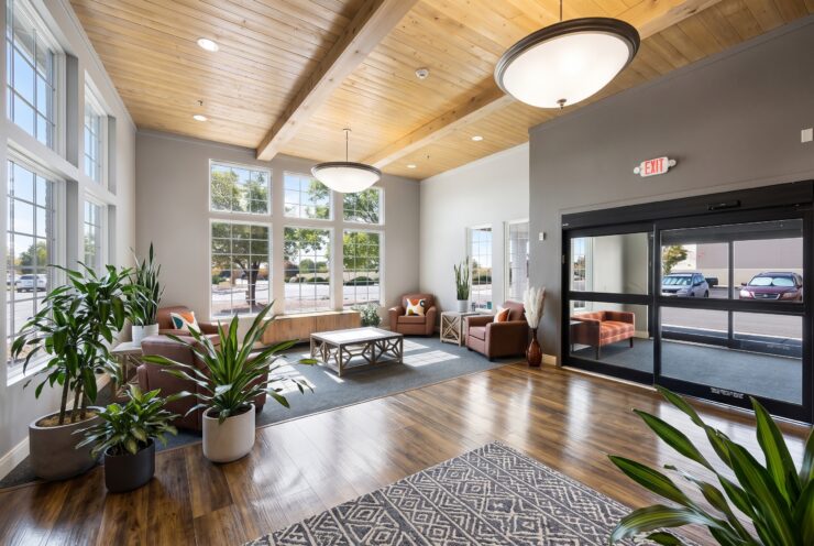 Bright lounge with large windows, comfortable chairs, plants, and warm wooden accents.
