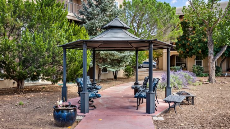 Shaded outdoor seating area surrounded by trees and greenery at a welcoming retirement community.