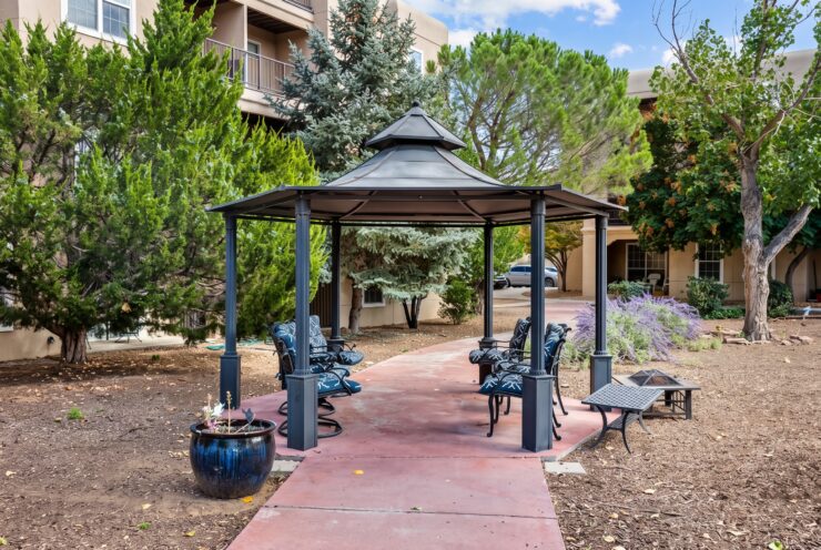 Shaded outdoor seating area surrounded by trees and greenery at a welcoming retirement community.