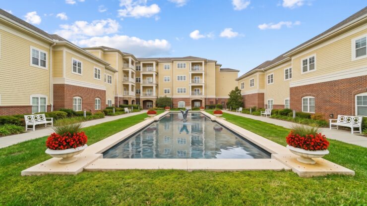 Sunlit courtyard with water feature, benches, and vibrant flowers in a welcoming community space.