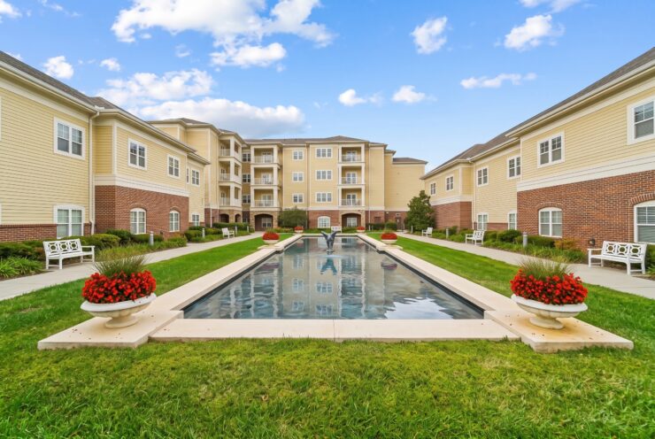 Sunlit courtyard with water feature, benches, and vibrant flowers in a welcoming community space.