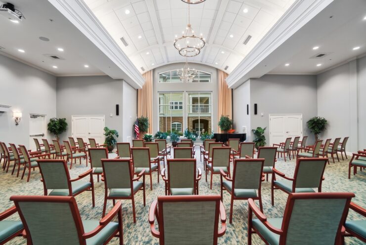Spacious entertainment room with arranged seating, natural light, and elegant chandeliers for community events.