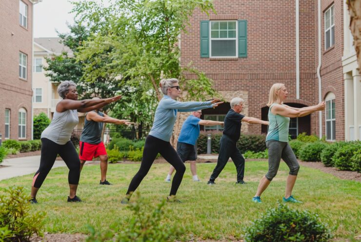 Seniors enjoying a group exercise class outdoors on a sunny day in a garden courtyard.