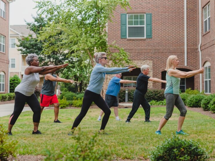 Seniors enjoying a group exercise class outdoors on a sunny day in a garden courtyard.