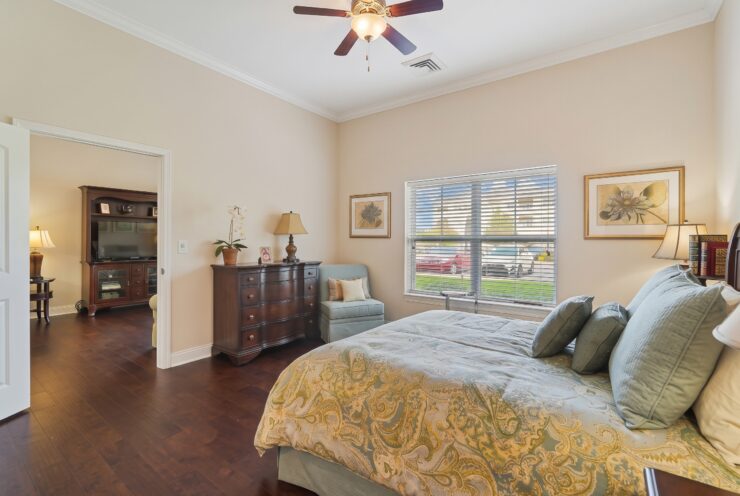 Sunlit bedroom with plush bedding, comfortable seating, and warm wood furnishings.