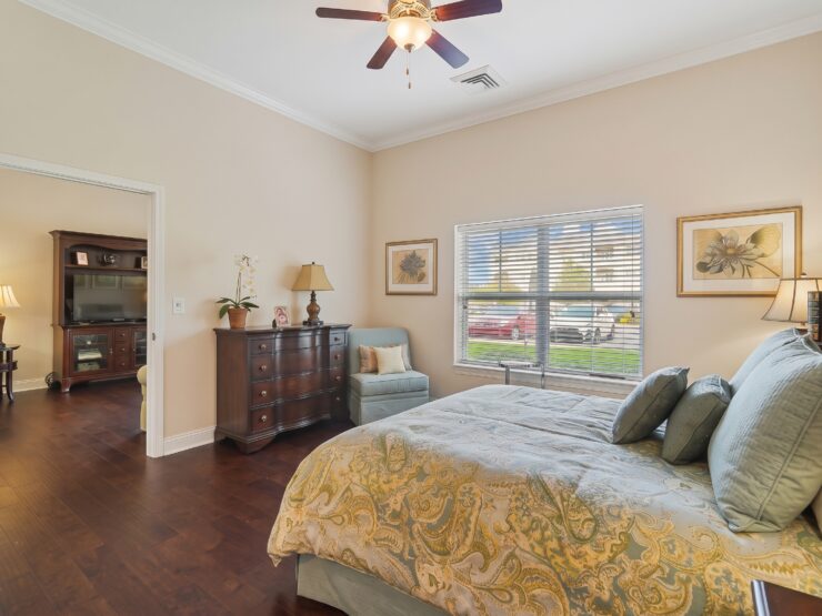 Sunlit bedroom with plush bedding, comfortable seating, and warm wood furnishings.