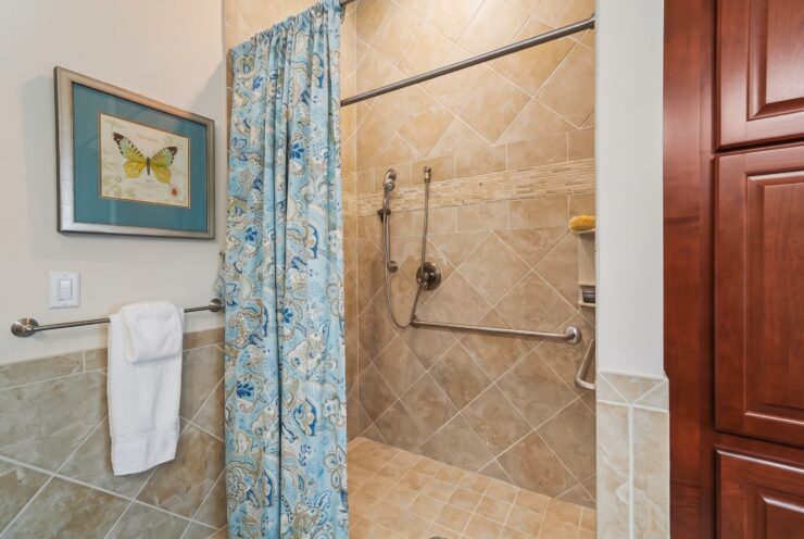 Spacious and accessible shower area with decorative curtain, warm tile, and supportive handrails.