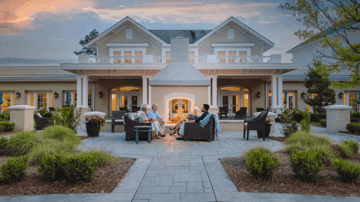 Seniors enjoying warm conversation around an outdoor fireplace in a welcoming community setting.