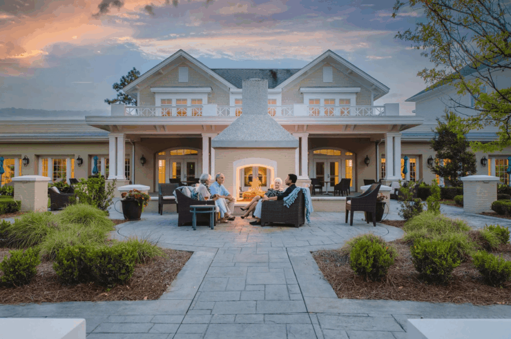 Seniors enjoying warm conversation around an outdoor fireplace in a welcoming community setting.