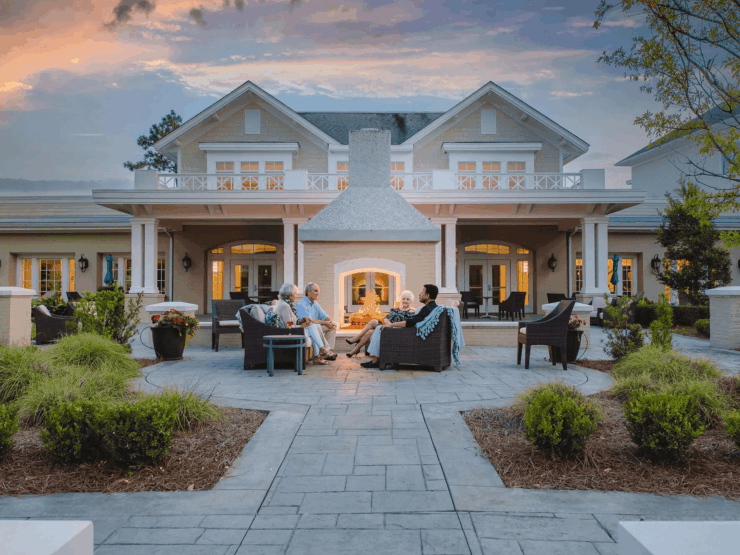 Seniors enjoying warm conversation around an outdoor fireplace in a welcoming community setting.