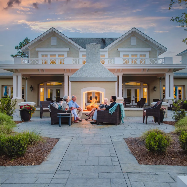 Seniors enjoying warm conversation around an outdoor fireplace in a welcoming community setting.
