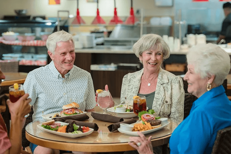 Seniors enjoying a lively meal together, sharing smiles and conversation in a bright dining area.