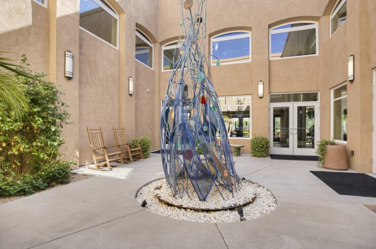 Sunlit courtyard with modern sculpture, rocking chairs, and inviting entry for social gathering.