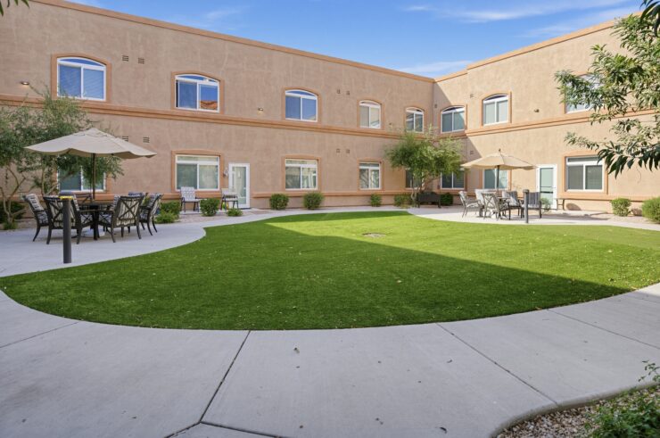 Sunny courtyard with seating areas and umbrellas surrounded by a welcoming retirement community building.