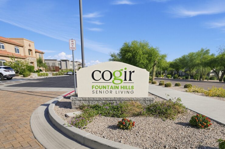 Welcoming entrance to a senior living community with landscaped gardens and sunny skies.