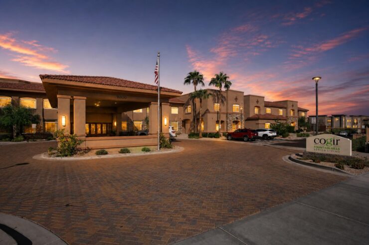Senior living community entrance with warm lighting and a welcoming sunset sky.