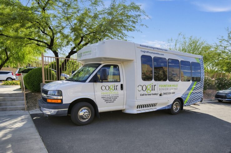 Shuttle bus parked outside senior living community surrounded by trees and clear skies.