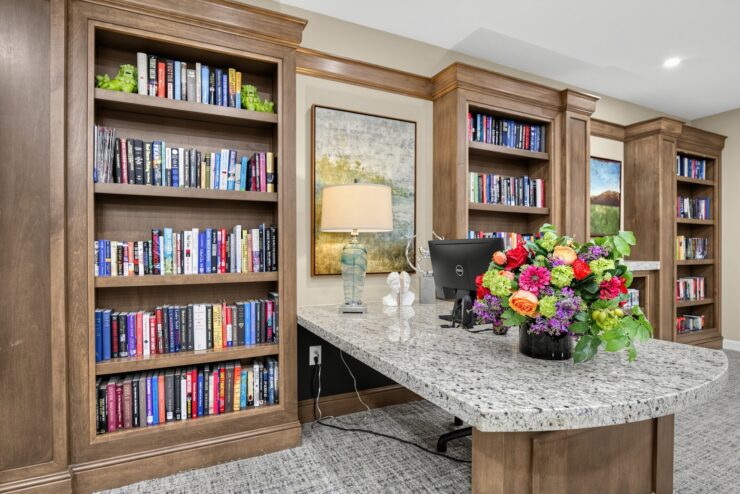 Welcoming library area with wooden bookshelves, a granite desk, and vibrant fresh flowers.