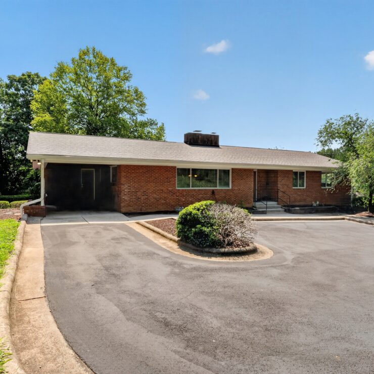 Single-story brick building surrounded by lush trees and well-maintained landscaping under a clear sky.