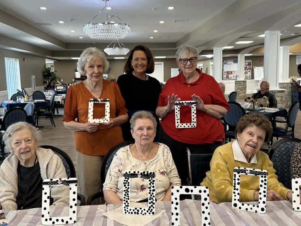 Seniors gather in a sunny crafts room, proudly displaying their decorated photo frames.