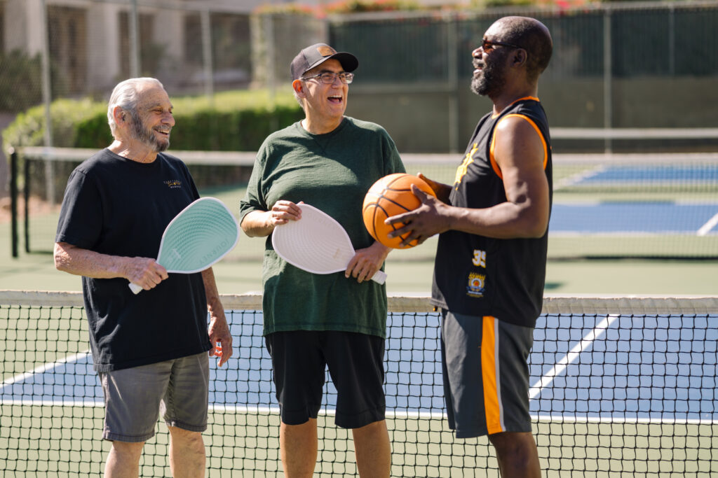 Three seniors smiling and chatting on a sports court, enjoying an active community setting.