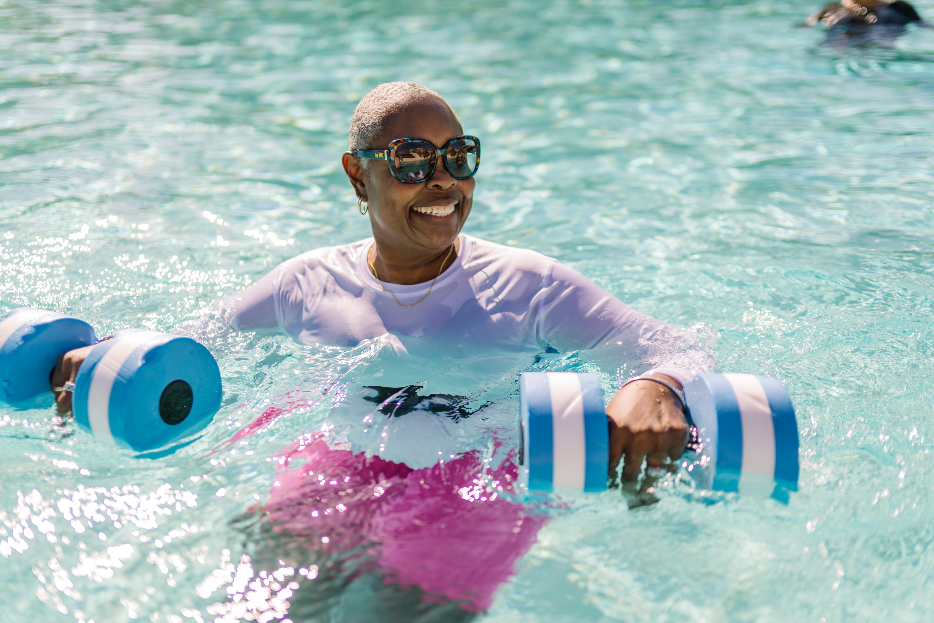 Senior woman smiling and enjoying water exercise with foam dumbbells in a sunny pool setting
