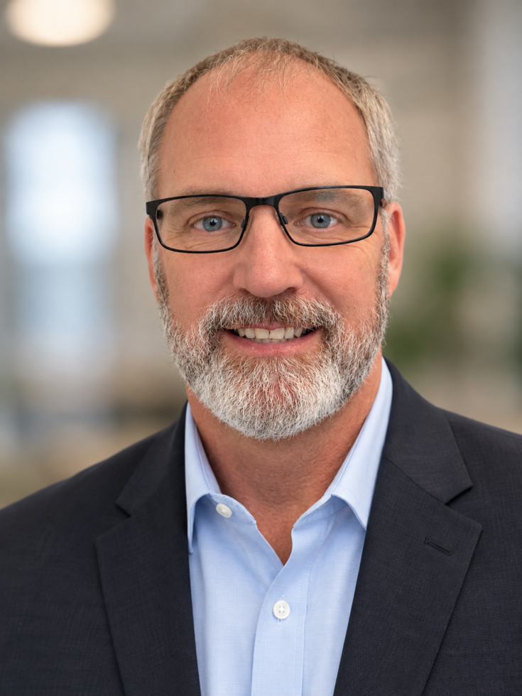 Friendly man with glasses and a beard smiling in a bright, welcoming community setting.