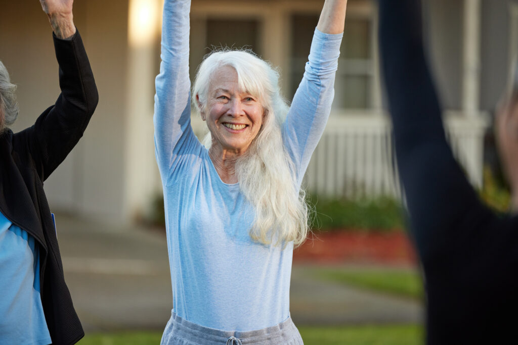 Senior woman joyfully raising arms during outdoor group exercise in a welcoming community setting
