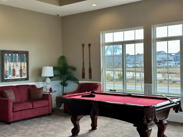 Lounge area with pool table, comfortable seating, and large windows overlooking a peaceful neighborhood.