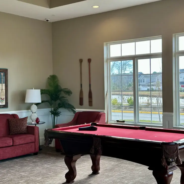 Lounge area with pool table, comfortable seating, and large windows overlooking a peaceful neighborhood.