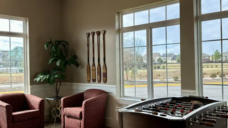 Bright common area with plush chairs, foosball table, and large windows overlooking the neighborhood.