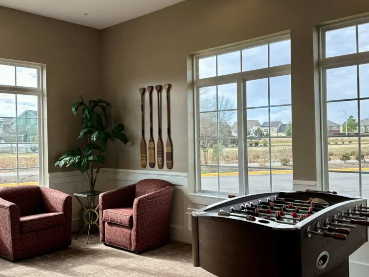 Bright common area with plush chairs, foosball table, and large windows overlooking the neighborhood.