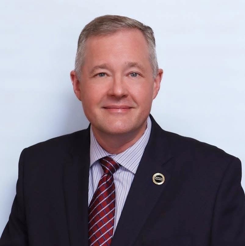 Professional man in suit smiling warmly, reflecting a welcoming and caring community.