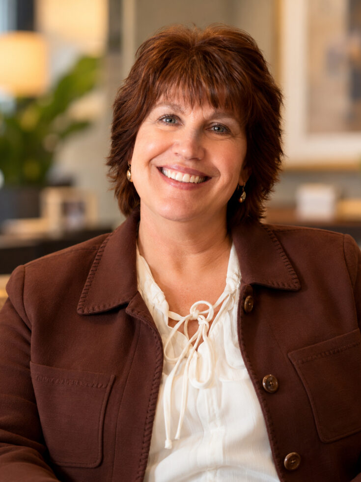 Warm and approachable woman smiling in a welcoming, home-like community setting.