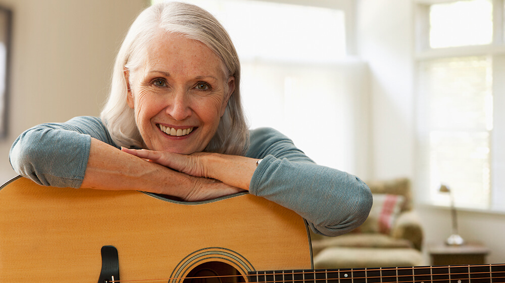 Woman smiles and rests her head on acoustic guitar