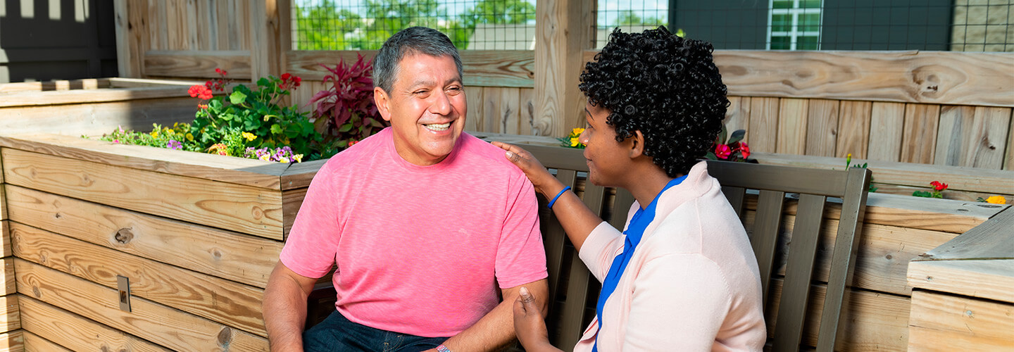 Staff member speaks with senior living resident on outdoor deck chair