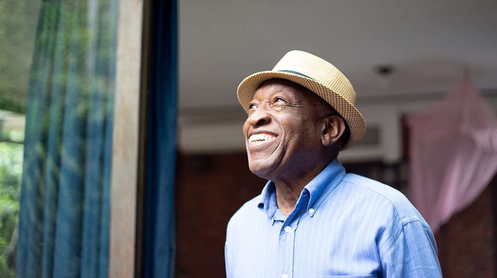 Older gentleman in stylish hat smiles in the sunlight