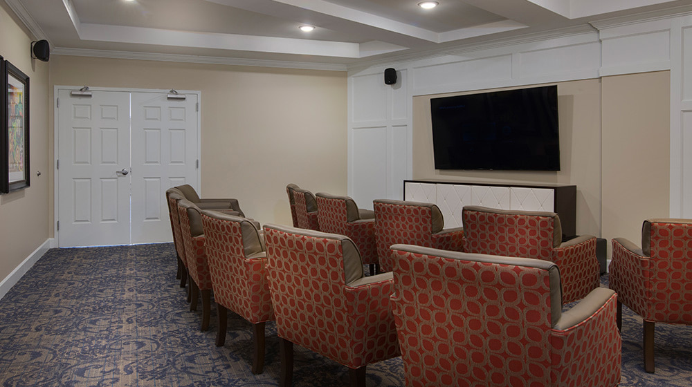 Theater room at at The Georgian Lakeside, with rows of comfy lounge chairs all facing a large TV mounted on the wall