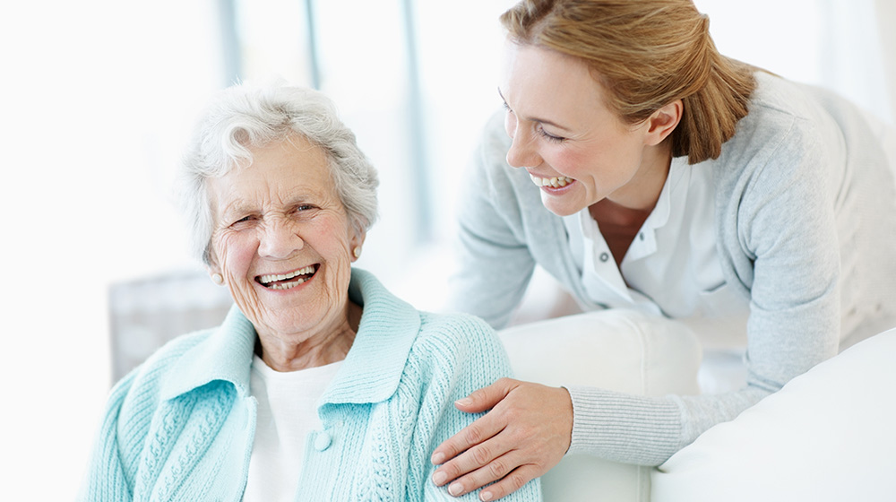 Smiling woman leaning over the shoulder of a senior woman