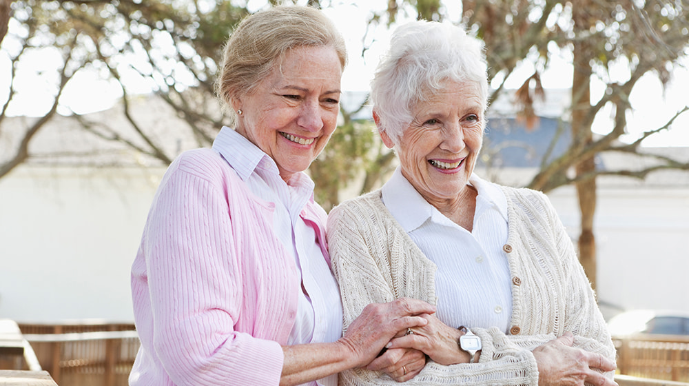 Two senior women smiling together outdoors.