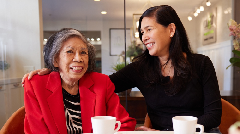 Senior woman smiling with her daughter while drinking coffee.